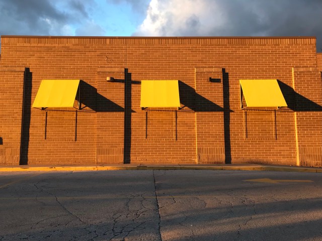 Three yellow-green awnings casting slanted shadows on an industrial brick wall