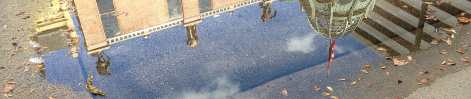 Grohmann Museum reflected in a puddle on a sunny day