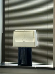 Squat, square black lamp with white shade against Venetian blinds on a sunny day