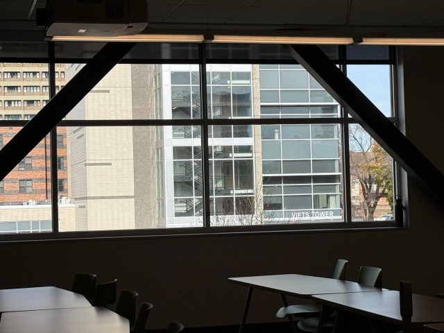A view of a glass-walled dormitory's exterior looking out a wide window from the interior of a classroom