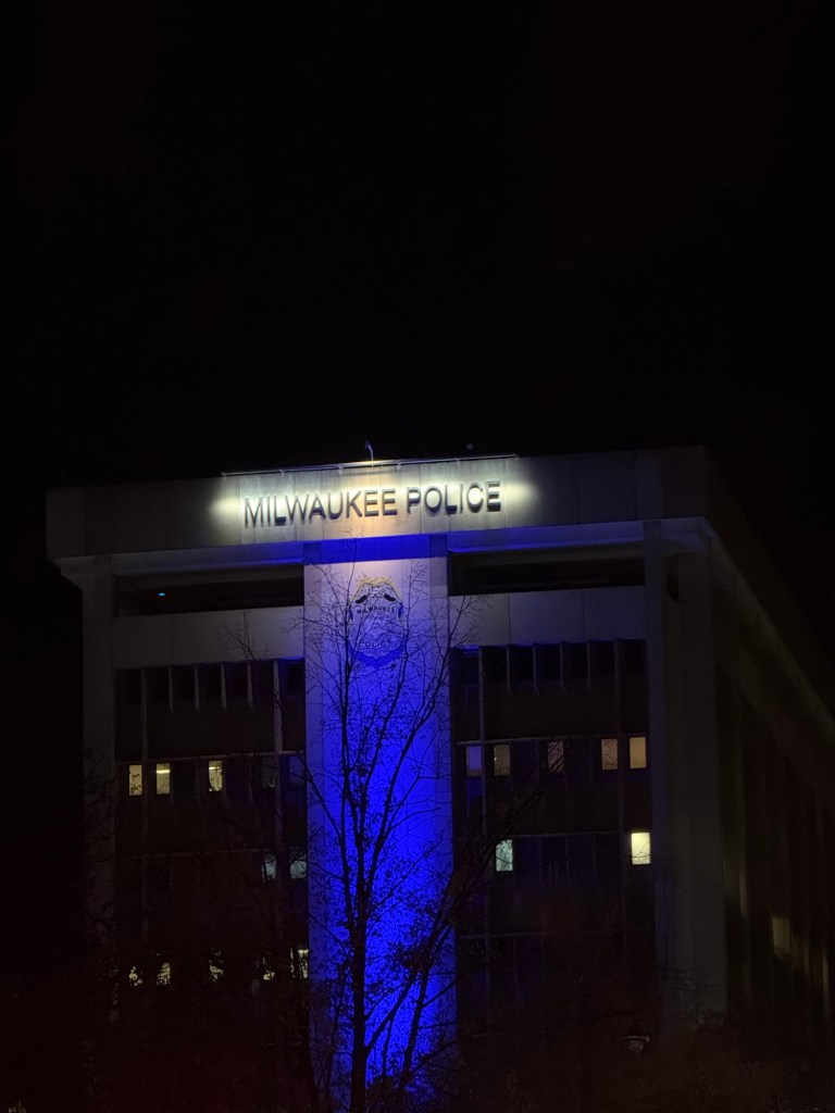 Milwaukee Police Department District 1 & Administration building, at night, with blue light and words “MILWAUKEE POLICE”